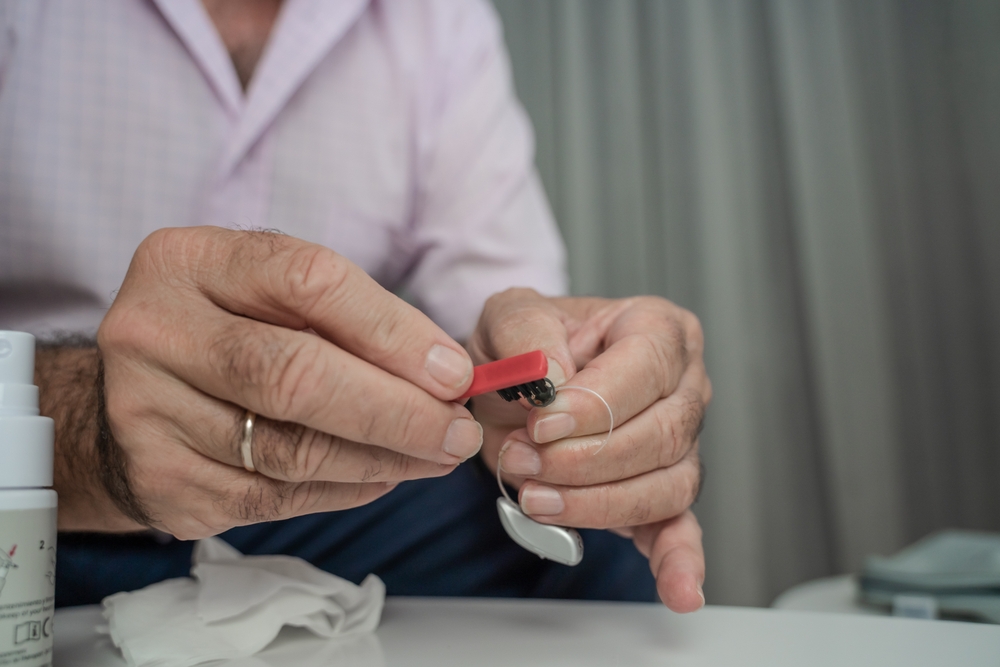 A person wearing a light pink shirt holds a red dental instrument in one hand and a dental implant in the other, preparing for a dental procedure.