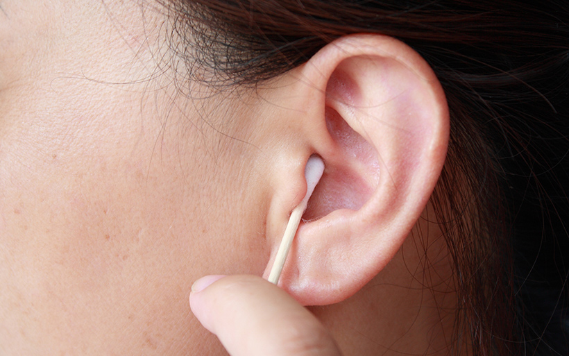 A person is cleaning their ear with a cotton swab, gently inserting it into the ear canal.