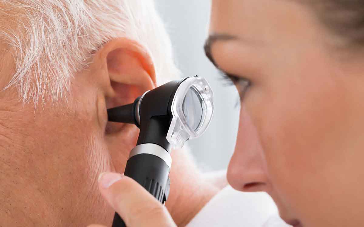 A healthcare professional uses an otoscope to examine the ear of an older adult with gray hair during a medical checkup.