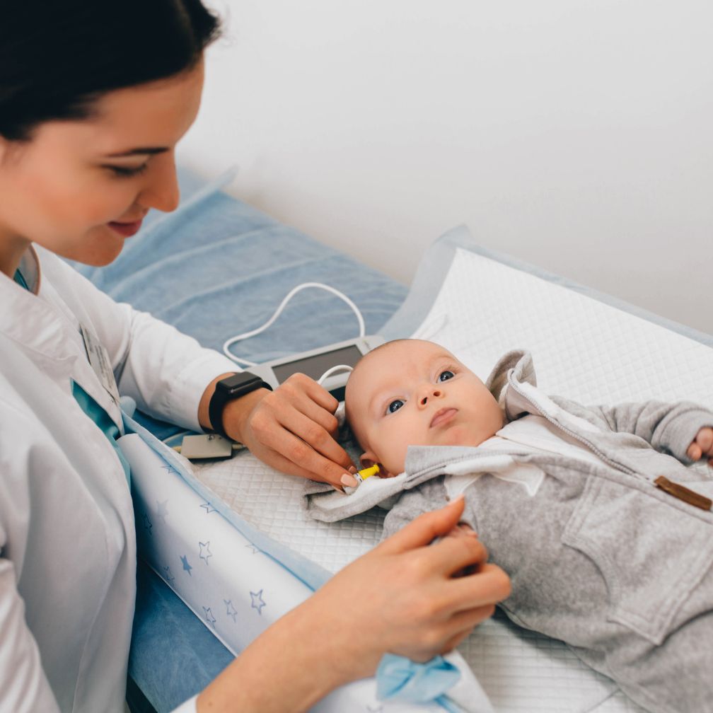 A healthcare professional tests a babys hearing using small earphones while the baby lies on a changing table, looking up calmly.